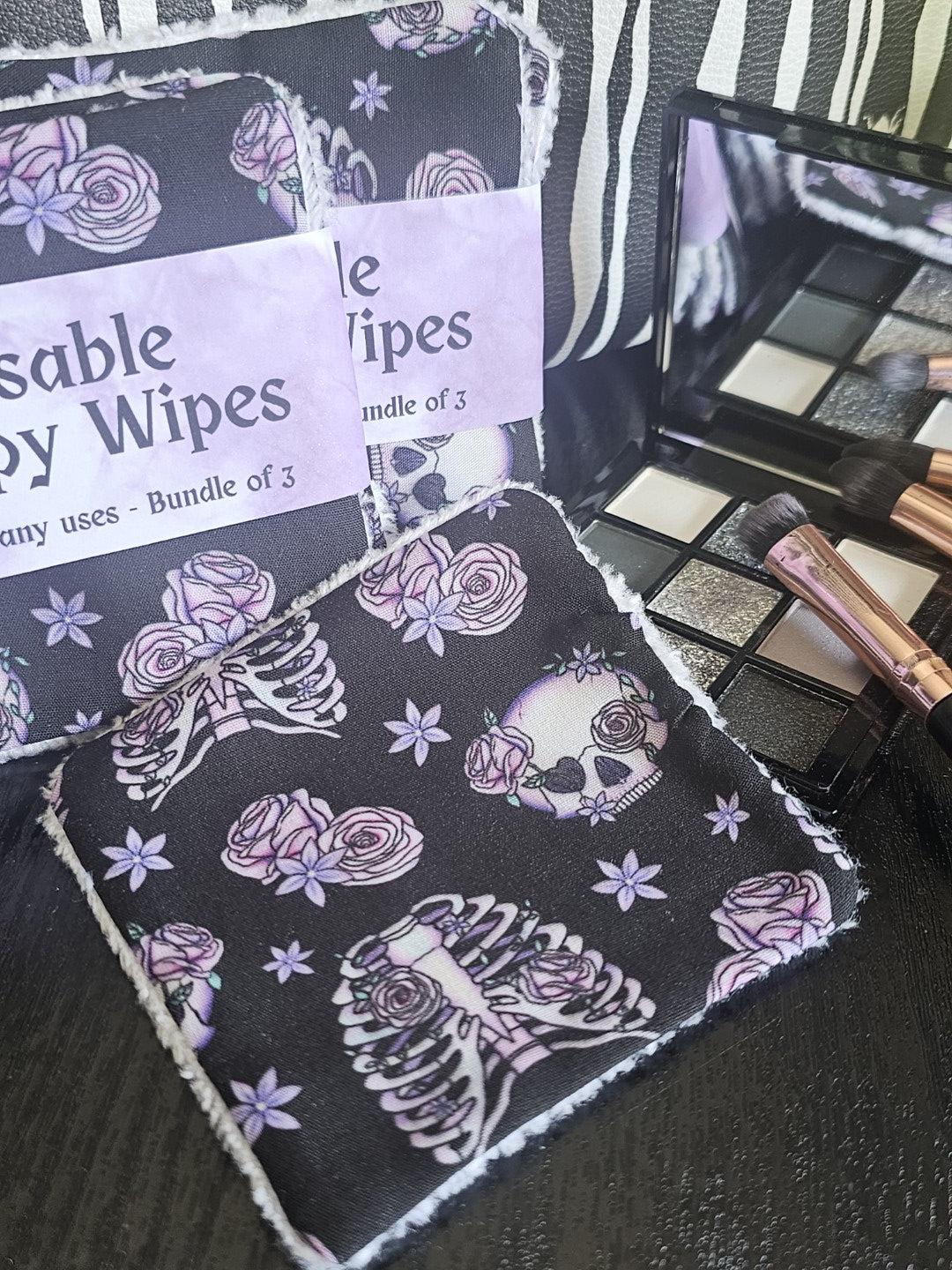 Reusable makeup wipes with skeleton and rose design on a black surface with makeup products.