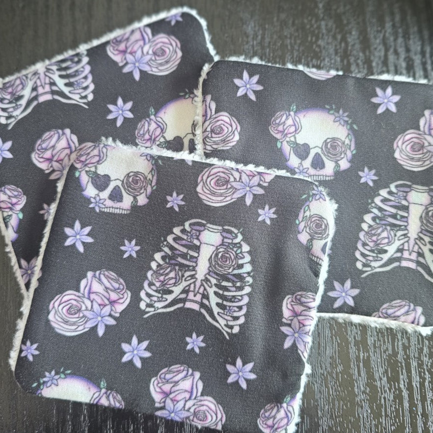 Three scrappy wipes with skull, rose and ribcage pattern on a dark surface