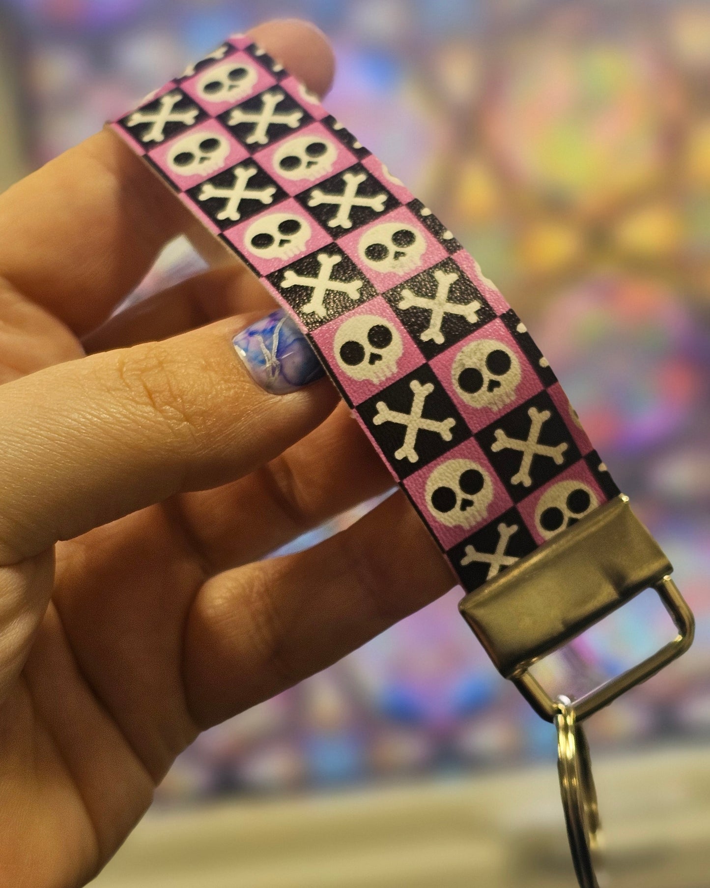 Keychain with Black and Pink skull and crossbones pattern held by a hand against a colourful blurred background