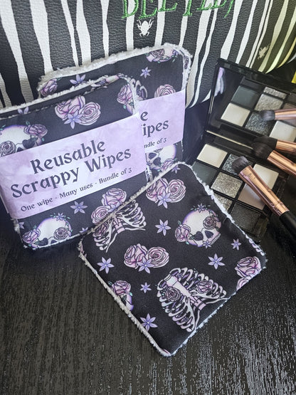 Reusable wipes with a skull, ribcage and floral design on a dark surface with makeup brushes and eyeshadow palate 