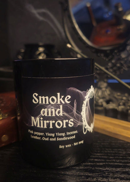 Candle labeled 'Smoke and Mirrors' with mentions of Pink pepper, ylang ylang, incense, leather and sandlewood. Set on a dark background