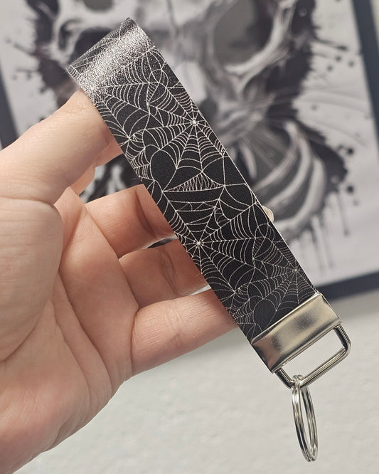 Keychain with spider web design held by a hand against a blurred background