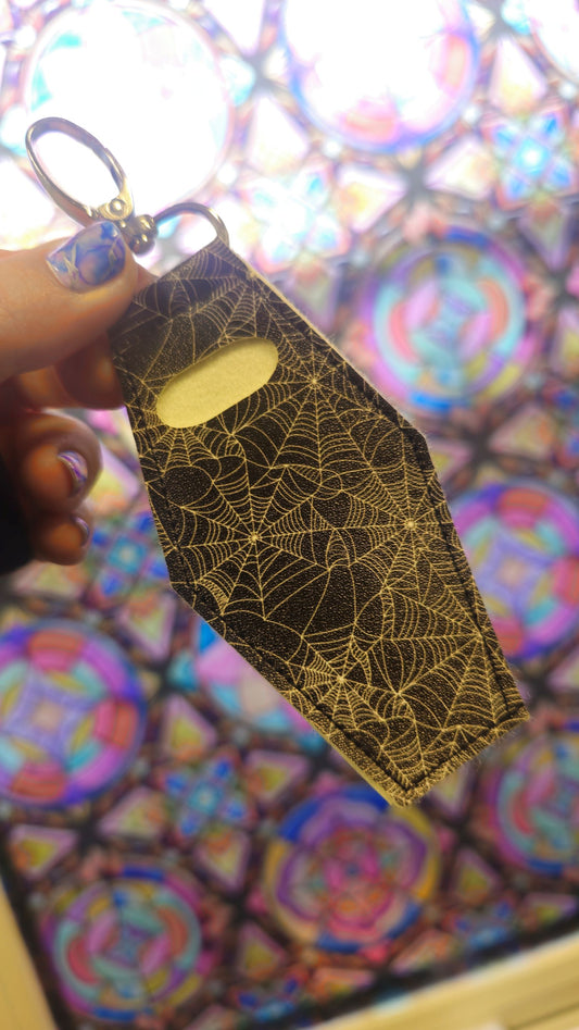 Coffin-shaped lip gloss holder keychain in black spiderweb print leatherette with stainless steel lobster clasp.