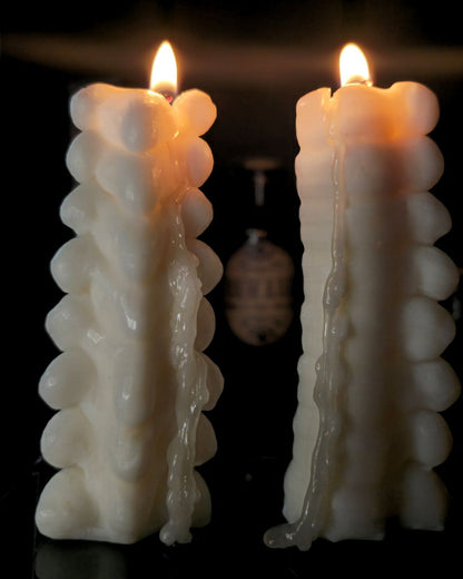 Two Spine shaped candles, lit and dripping with wax. Set against a dark but candle lit background 