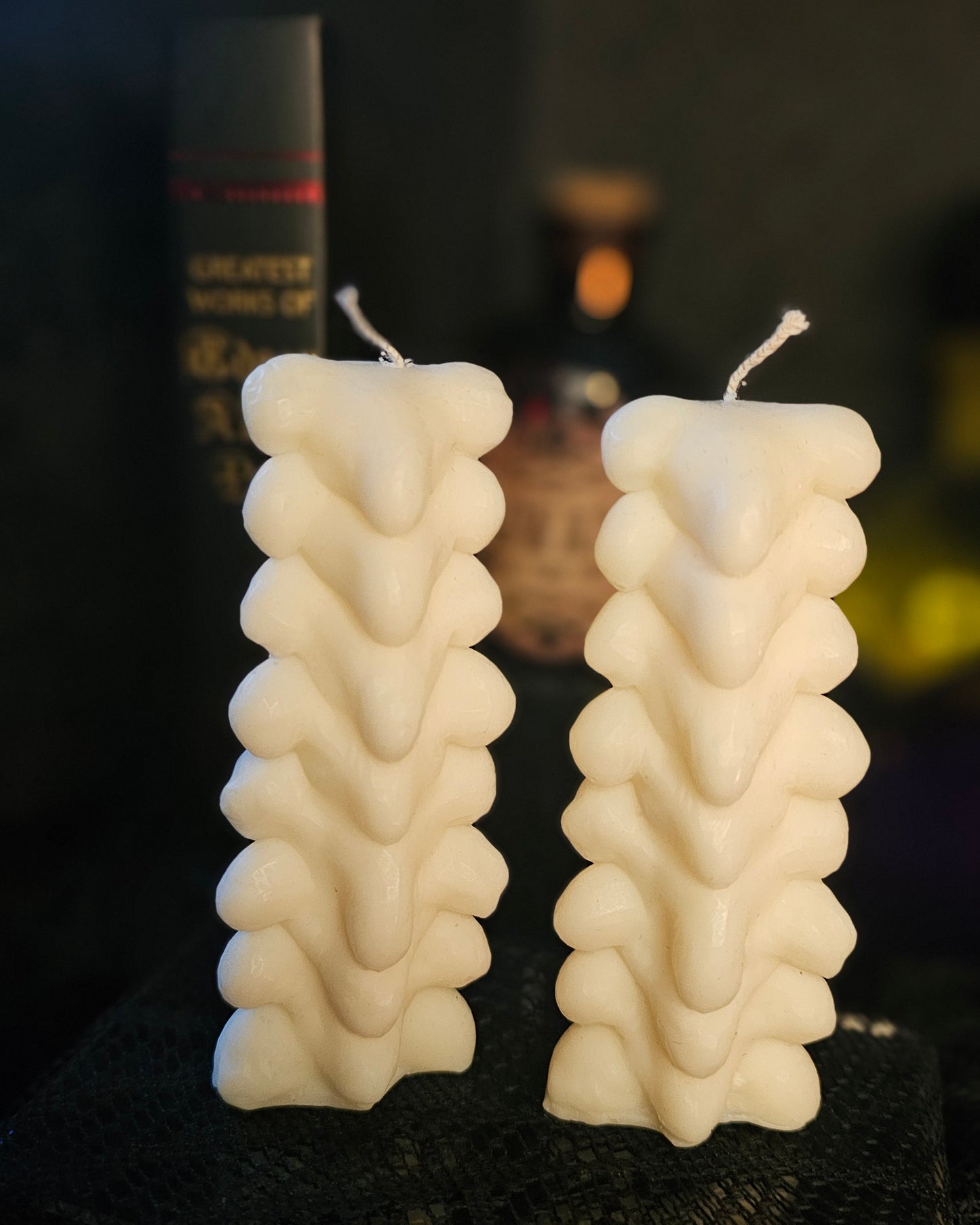 Two white spine shaped candles on a dark surface with a blurred background