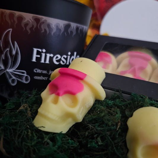 A skull-shaped wax melt with a yellow and red colouring, labeled 'Fireside' with citrus, jasmine, tobacco, leather, raspberry, cedarwood, musk, amber, and vetiver scents.
