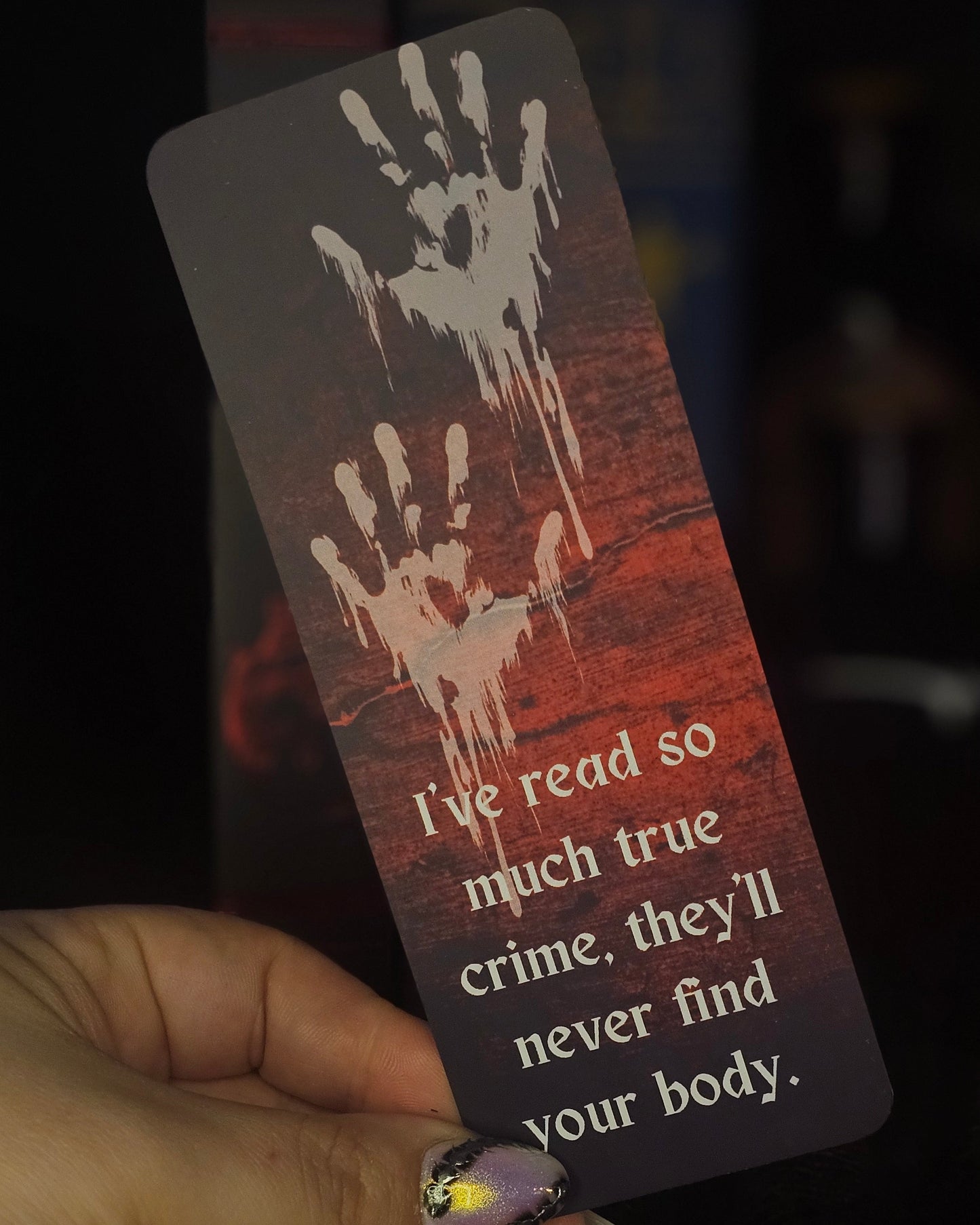 A bookmark with a blood-red background featuring handprint illustrations and the text 'I've read so much true crime, they'll never find your body.'.