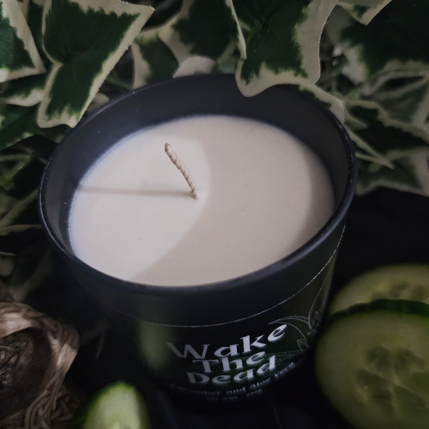 Candle in a black container sitting on a dark surface with cucumber slices 