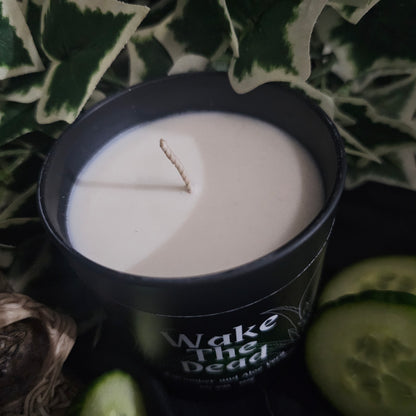 Candle in a black container sitting on a dark surface with cucumber slices 