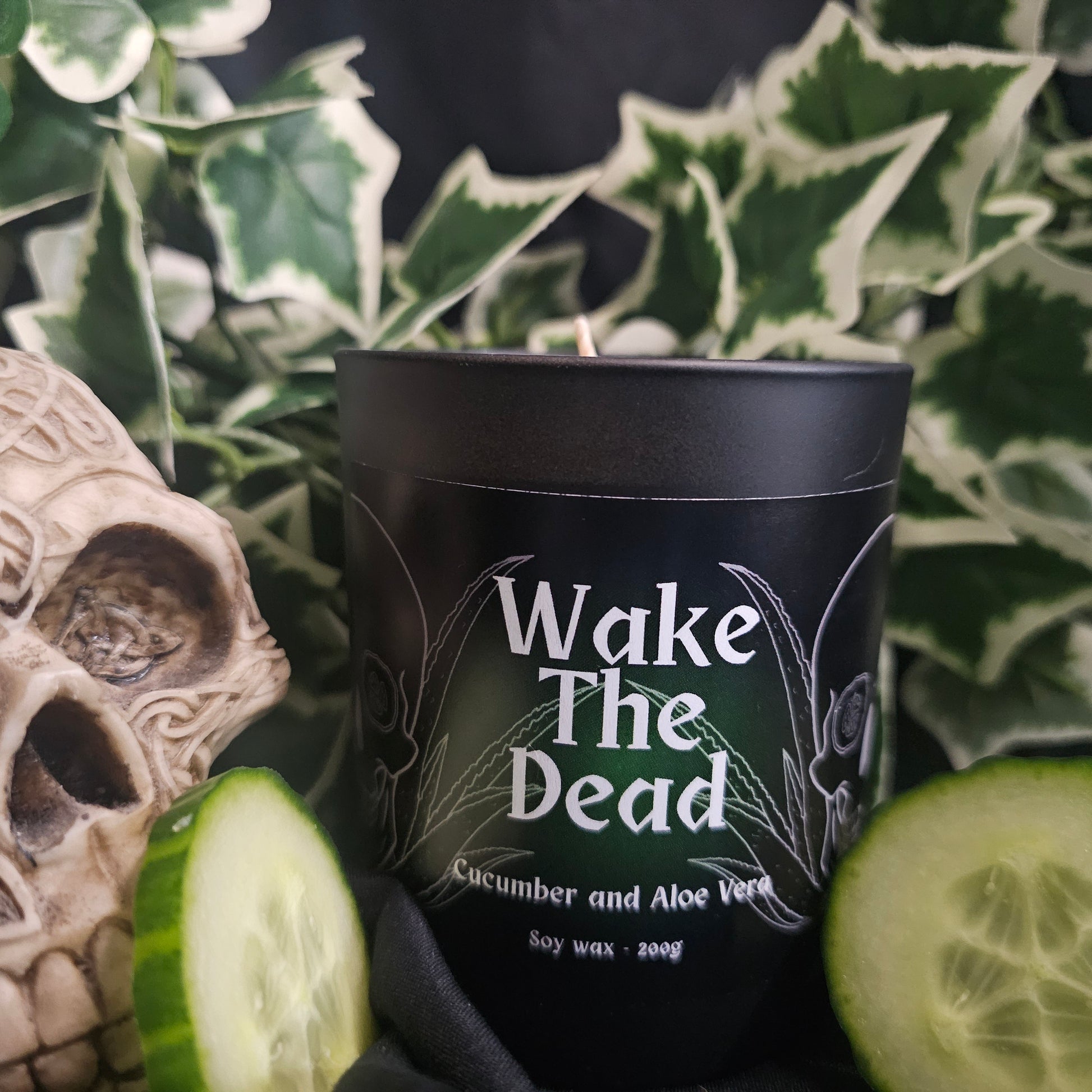 Black candle container with 'Wake The Dead' text and cucumber slices, with a decorative skull in the background.