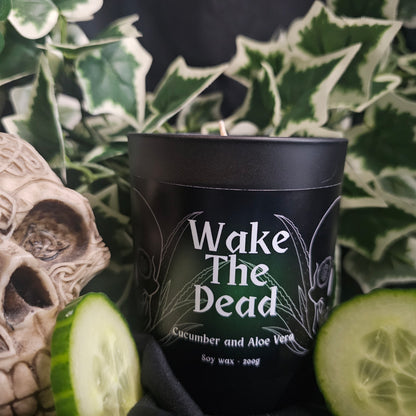 Black candle container with 'Wake The Dead' text and cucumber slices, with a decorative skull in the background.