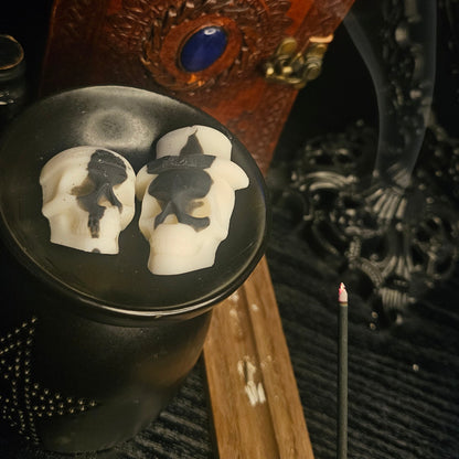 Skull-shaped wax melts on a black melt burner with incense and intricate background