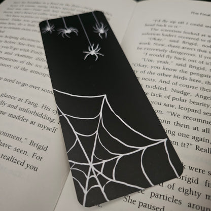 Black spider web and spider design on a bookmark, placed on an open book.