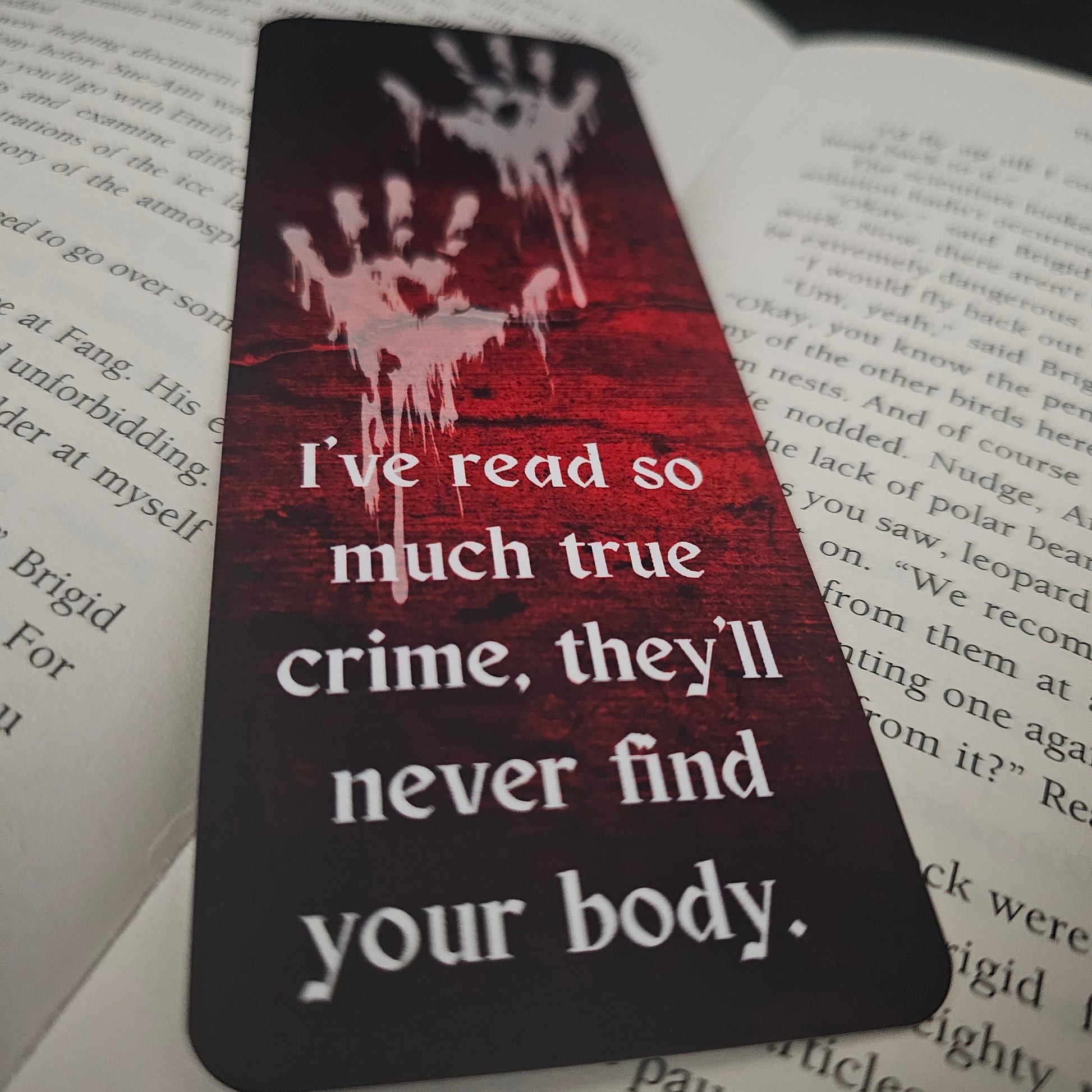 A bookmark with a blood-red background featuring handprint illustrations and the text 'I've read so much true crime, they'll never find your body.'.